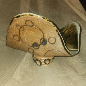 Könnte beinhalten: Ein Keramik-Serviettenhalter mit brauner Glasur und schwarzen Kreisdesigns. Der Halter hat eine abgerundete Form und einen kleinen Sockel.
