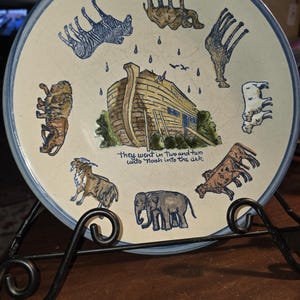 Könnte beinhalten: Dekorative Platte mit blauem Rand, die die Arche Noah und verschiedene Tierpaare zeigt. Die Platte enthält den Text "they went in two and two unto Noah into the ark". Gezeigte Tiere sind Zebras, Giraffen und Elefanten.