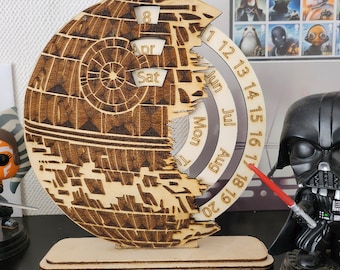 May include: A wooden calendar shaped like the Death Star from Star Wars. The calendar has a rotating dial with the months June, July, and August. The numbers 1 through 20 are printed on the dial. The calendar is on a wooden base.