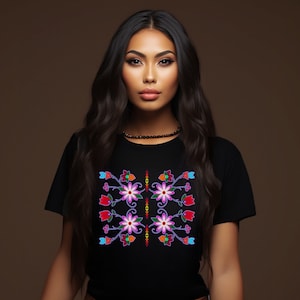 May include: Black t-shirt featuring a symmetrical floral design in pink, red, blue, and orange. The design includes stylized flowers and leaves. The model is wearing a brown belt and white pants.