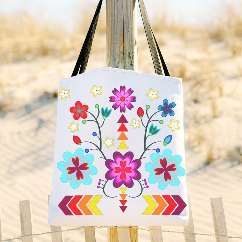 May include: White canvas tote bag with a colorful floral design featuring pink, red, blue, yellow, and green flowers. The flowers are arranged in a symmetrical pattern with a geometric design at the bottom.