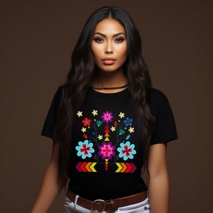 May include: A black t-shirt with a colorful floral embroidery design. The design features a central flower with pink, blue, and yellow petals, surrounded by smaller flowers and leaves in various colors. The embroidery is framed by a row of orange and yellow arrows.