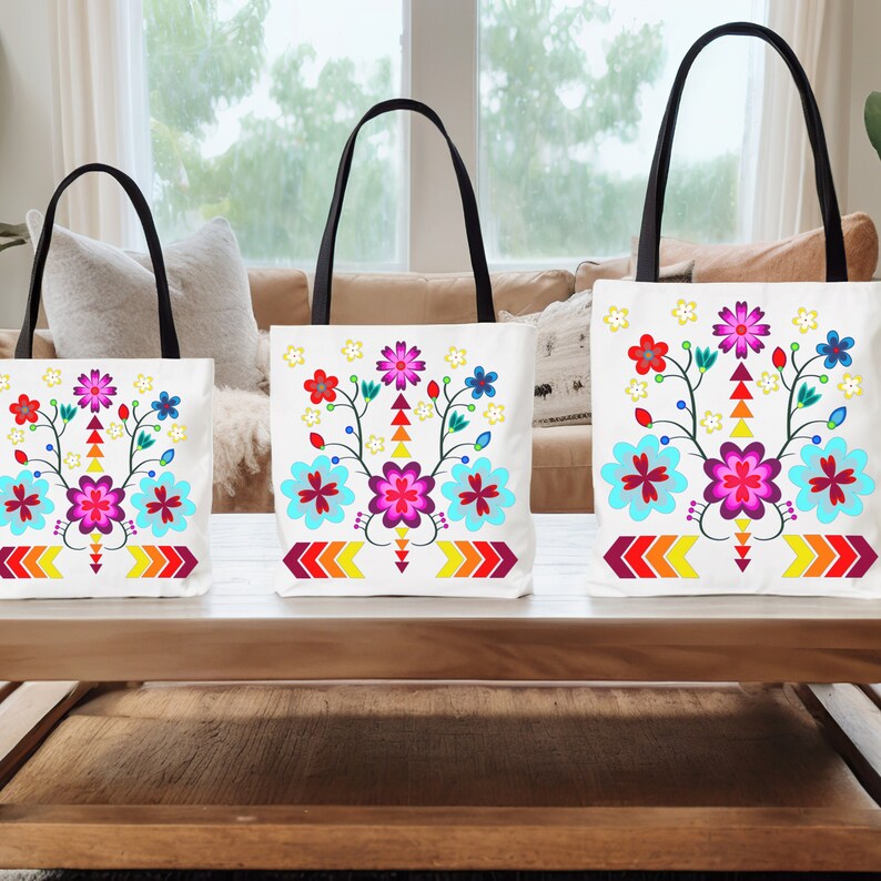 May include: Three white tote bags with black handles. Each bag features a colorful floral design with a central flower in shades of pink and purple. The floral design is surrounded by smaller flowers in yellow, blue, and red. The bottom of each bag has a row of yellow, orange, and red arrows.