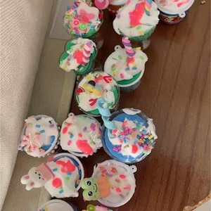 Könnte beinhalten: Eine Sammlung von bunten, dekorierten, Miniatur-Eisbechern. Jeder Becher ist mit verschiedenen Streuseln, Süßigkeiten und anderen Dekorationselementen verziert. Die Becher sind in einer Reihe auf einer Holzoberfläche angeordnet.