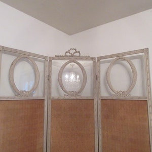 May include: A three-panel room divider with a light gray painted finish. Each panel features a large oval-shaped cutout with a decorative frame. The panels are made of wood and have a woven fabric backing.