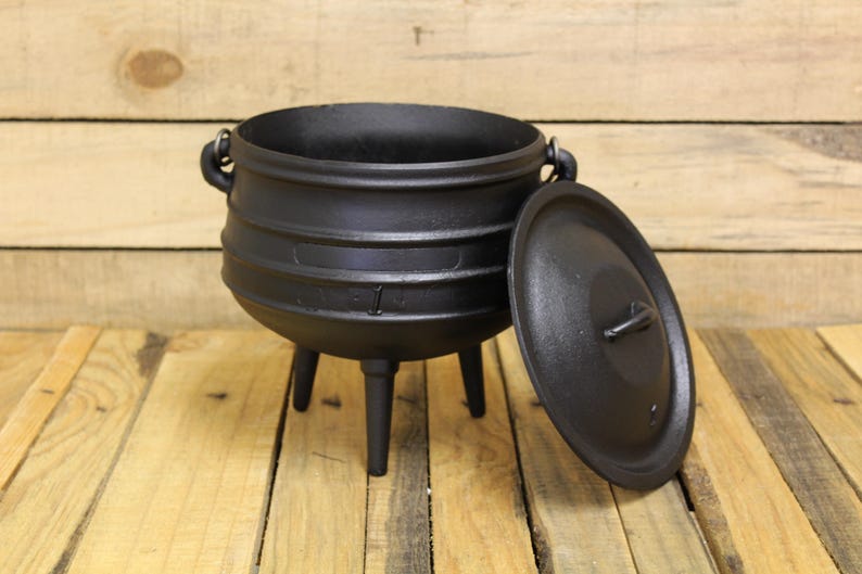 May include: A black cast iron pot with three legs and a matching lid. The pot features a rounded body with a wide opening, two side handles for lifting, and a central handle on the lid. The surface has a matte finish and a sturdy construction.
