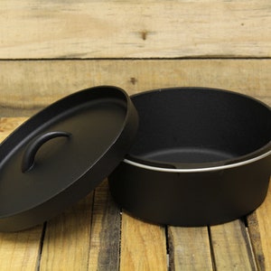 May include: A black cast iron Dutch oven with a matching lid. The lid is off to the side, revealing the interior of the pot. The pot has a silver handle and is sitting on a wooden surface. This cookware is ideal for camping and outdoor cooking.