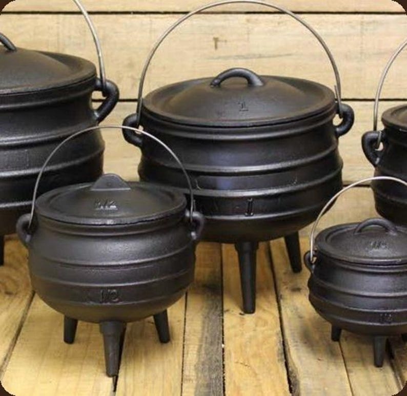May include: A collection of black cast iron pots with lids, each featuring three legs and a wire handle. The pots have a rounded belly shape and are embossed with size markings such as 1/2 and 1, indicating their capacity in litres.