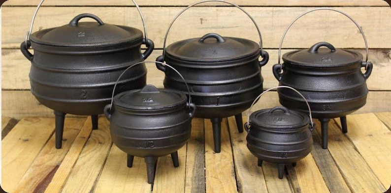 May include: A set of five black cast iron pots with lids, each featuring three legs and a wire handle. The pots vary in size and are arranged in a group, showcasing a rounded body design with horizontal ridges on the exterior surface.