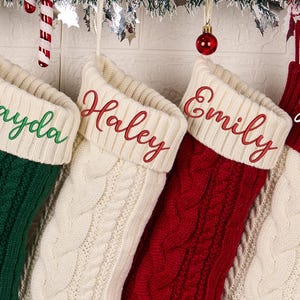 以下が含まれることがあります： クリーム、緑、赤のケーブルニットのクリスマスストッキング5つ。それぞれに名前が刺繍されています。Chase、Jayda、Haley、Emily、Kevin。お祝いのホリデーデコレーション。