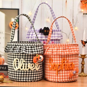 May include: Three cylindrical fabric baskets with handles and ruffled tops. One is black and white gingham with the name Oliver, one is orange and white gingham with the name Sophia, and one is purple and white gingham with a bat applique.