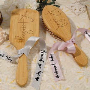 May include: Two wooden hairbrushes with engraved names, tied with ribbons. One brush is rectangular with "Audrey" engraved, the other is oval with "Rachel". Ribbons say "Friend for life" and "Bridesmaid today".