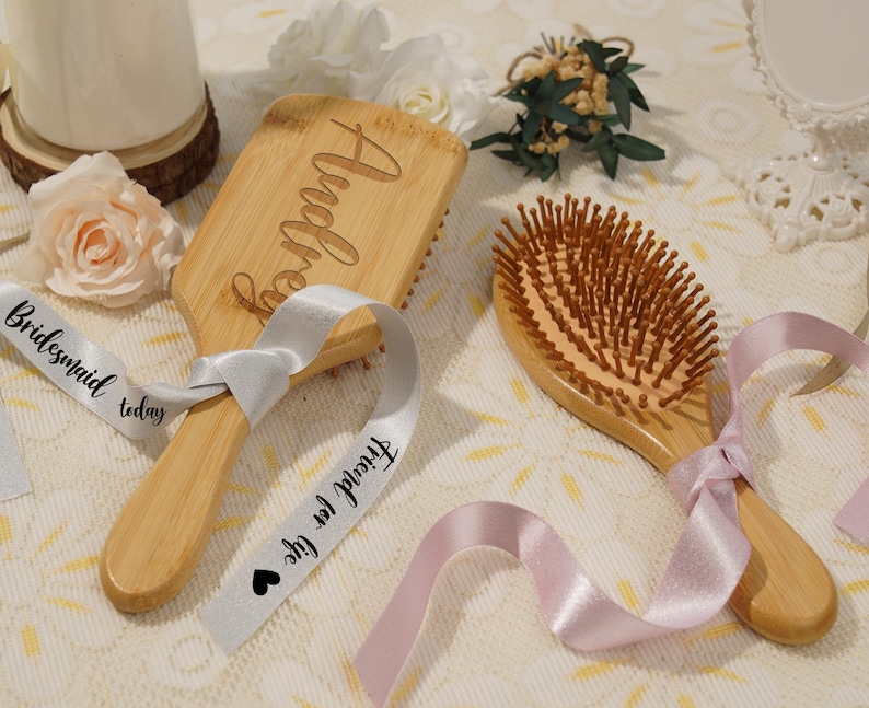 May include: Two wooden hairbrushes with light brown bristles and handles. One brush is engraved with the name "Audrey". Both brushes are adorned with satin ribbons. One ribbon reads "Bridesmaid today" and "Friend for life".