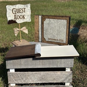 Peut inclure: Un ensemble de livre d'or comprenant un panneau en bois avec le texte GUEST BOOK et un album photo assorti avec une couverture en peau de vache et des accents en bois fonc&eacute;. La couverture est grav&eacute;e SEPTEMBER 5, 2026, avec des pages vierges.
