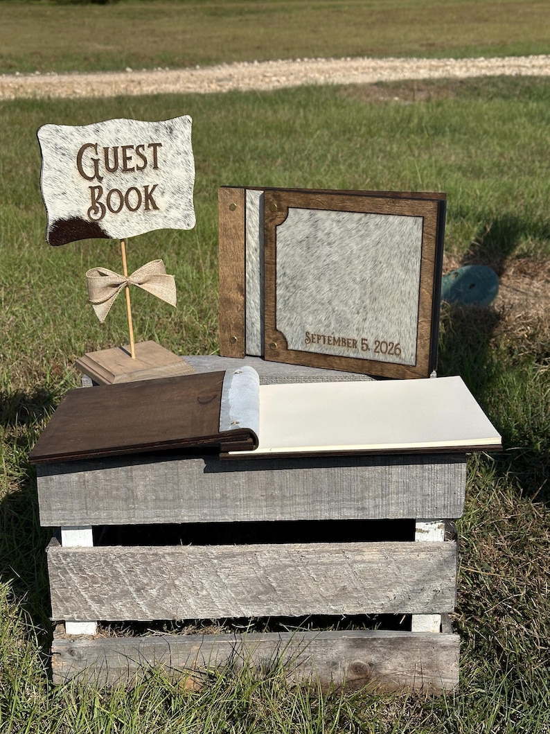 Peut inclure: Un ensemble de livre d'or comprenant un panneau en bois avec le texte GUEST BOOK et un album photo assorti avec une couverture en peau de vache et des accents en bois fonc&eacute;. La couverture est grav&eacute;e SEPTEMBER 5, 2026, avec des pages vierges.