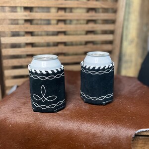 Pu&ograve; includere: Due portabicchieri neri con cuciture bianche e un design decorativo. I portabicchieri sono realizzati in un materiale simile alla pelle scamosciata e sono progettati per mantenere le bevande fredde. Le lattine sono argentate.
