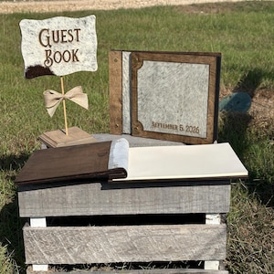 Peut inclure: Un panneau livre d'or avec une texture en peau de vache et le texte GUEST BOOK, accompagn&eacute; d'un livre d'or assorti avec une reliure en bois fonc&eacute;, une couverture en peau de vache et le texte grav&eacute; SEPTEMBER 5, 2026, et un livre ouvert.