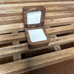 May include: A small, wooden ring box with a hinged lid. The box is made of dark wood and has a light brown velvet interior.