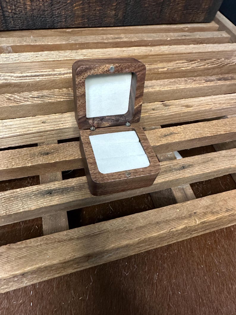 May include: A small, wooden ring box with a hinged lid. The box is made of dark wood and has a light brown velvet interior.