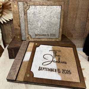 Peut inclure: Deux albums photo carr&eacute;s en bois avec des panneaux en peau de vache. L'album du haut a une peau grise et blanche avec le texte SEPTEMBER 5, 2026. L'album du bas a une peau brune et blanche avec le texte The Jenkins et SEPTEMBER 5, 2026.