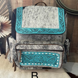 May include: A backpack crafted from gray and white speckled cowhide leather, featuring a top flap and front pocket accented with bright turquoise leather panels. The turquoise sections are embossed with intricate floral scrollwork and white stitching.