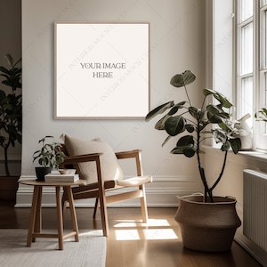 Puede incluir: Una silla de madera clara con un cojín beige se encuentra en una habitación con una ventana grande y una planta en maceta. Un cuadro enmarcado cuelga de la pared sobre la silla. El marco del cuadro es de madera clara y la imagen está en blanco.