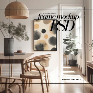 May include: A black framed abstract painting with beige and gray circles on a beige background hangs on a white wall in a dining room. The room has a wooden table with four chairs, a vase with dried branches, and a wicker pendant light.