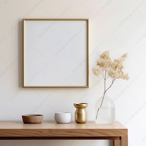 Könnte beinhalten: Ein goldfarbener Bilderrahmen steht auf einem Holztisch mit einer Vase mit Trockenblumen, einer kleinen Schale und einer goldenen Vase.