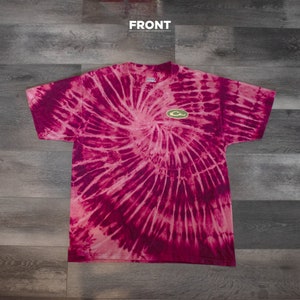 May include: A pink and white tie-dye t-shirt with a green duck logo on the front. The shirt has a spiral pattern.