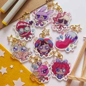 Pode incluir: Uma cole&ccedil;&atilde;o de sete chaveiros de acr&iacute;lico transparente com personagens de desenhos animados coloridos de olhos grandes, cada um preso a um fecho dourado em forma de estrela. Os designs incluem v&aacute;rias figuras com vibrantes tons de rosa, roxo, azul e vermelho.