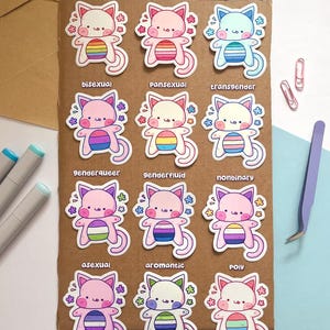 May include: A collection of colorful cat stickers, each with a different pride flag design. The stickers feature a cute cat illustration with a rainbow, lesbian, gay, bisexual, pansexual, transgender, genderqueer, genderfluid, nonbinary, asexual, aromantic, and poly flag.
