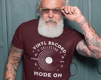 Op de afbeelding: Een maroon t-shirt met een wit grafisch ontwerp van een vinylplaat met de tekst "Vinyl Record Collector Since 1975 Mode On".