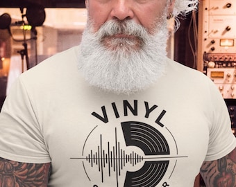 Puede incluir: Camiseta color crema con un gráfico negro de un disco de vinilo, ondas de sonido y el texto "VINYL SOUNDS BETTER". La camiseta la lleva una persona con barba blanca.