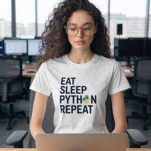 May include: White t-shirt with the text "EAT SLEEP PYTHON REPEAT" in navy blue, with a yellow and blue Python logo. The shirt is being worn by a person in an office setting.
