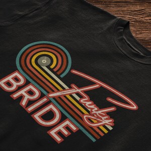 Può includere: Felpa nera con un design arcobaleno retrò e il testo "Bride" e "Funky" in bianco.