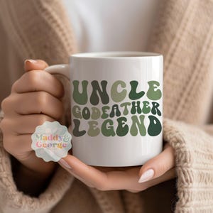 May include: White ceramic mug with the text "Uncle Godfather Legend" in green and brown retro-style lettering.