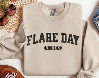 May include: A tan sweatshirt with the text "FLARE DAY VIBES" in black block letters.