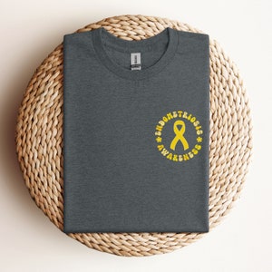 May include: A dark gray t-shirt with a yellow circle design that says "Endometriosis Awareness" with a yellow ribbon in the center.