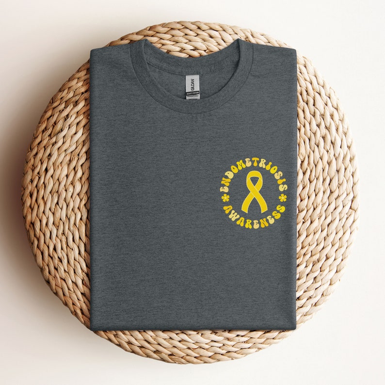 May include: A dark gray t-shirt with a yellow circle design that says "Endometriosis Awareness" with a yellow ribbon in the center.