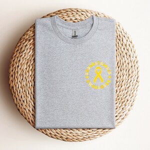May include: Gray t-shirt with a yellow ribbon and the text "ALBINISM AWARENESS" in a circle around the ribbon.