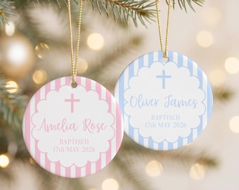 May include: Two round ceramic ornaments with gold hanging strings. One features pink stripes, a cross, and the text Amelia Rose BAPTISED 17th MAY 2026. The other has blue stripes, a cross, and the text Oliver James BAPTISED 17th MAY 2026.