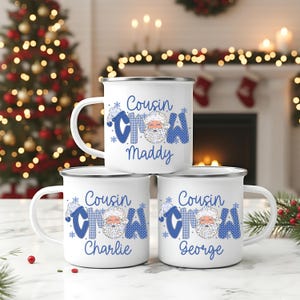 May include: Three white enamel mugs with silver rims are stacked. Each mug features the text "Cousin Snow" in blue, with a Santa Claus graphic and a personalized name. The mugs are Christmas-themed.
