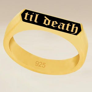 May include: Gold-colored ring with a black rectangular center. The text "til death" is inscribed in gold lettering on the black surface. The ring is stamped with "925".