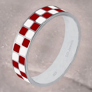 May include: A silver ring with a checkered pattern of red and white squares. The ring is marked with "DD Jewels" and "925". The ring is on a neutral background.