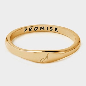 May include: A gold-colored ring with the word "PROMISE" engraved on the top. The ring has a smooth, polished finish and features a cursive letter "A" on the front.