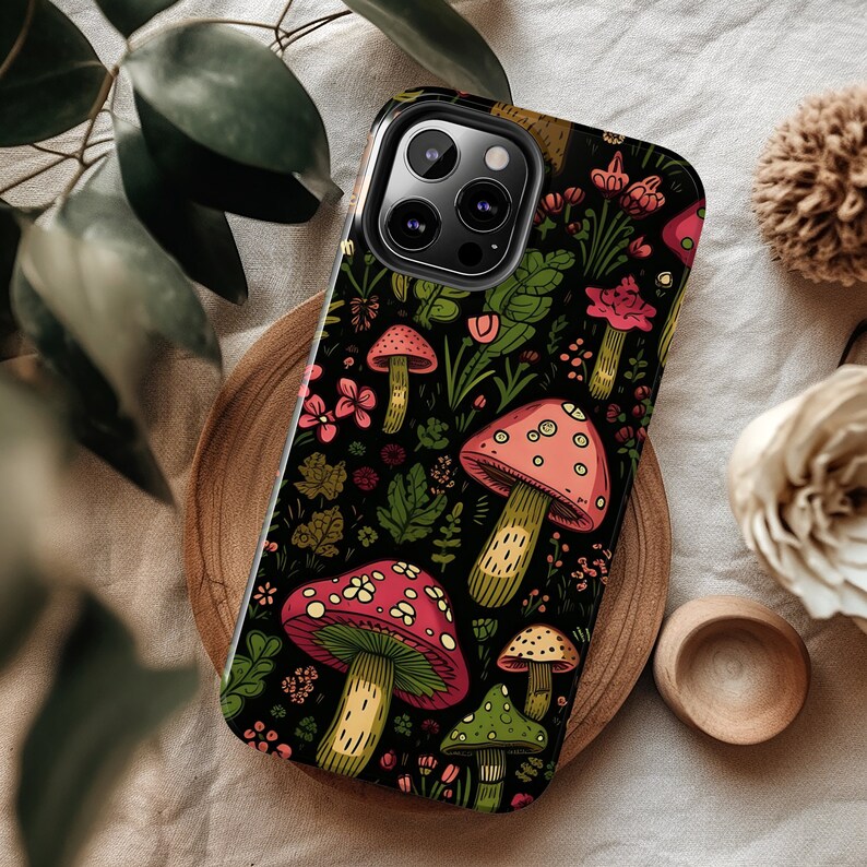 K&ouml;nnte beinhalten: Eine schwarze Handyh&uuml;lle mit einem bunten Pilz- und Blumendesign. Die H&uuml;lle hat einen Ausschnitt f&uuml;r das Kameraobjektiv und einen schwarzen Hintergrund.