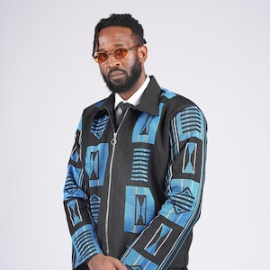 May include: Black zip-up jacket with blue geometric patterns. The jacket features a collar, long sleeves, and a silver zipper. The design includes rectangular and striped shapes in blue and white.