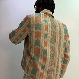 Puede incluir: Chaqueta beige con estampado geom&eacute;trico en naranja y verde azulado. El patr&oacute;n repite rayas verticales y formas de rombos. La chaqueta tiene cuello y mangas largas. La persona que lleva la chaqueta se ve por la espalda.