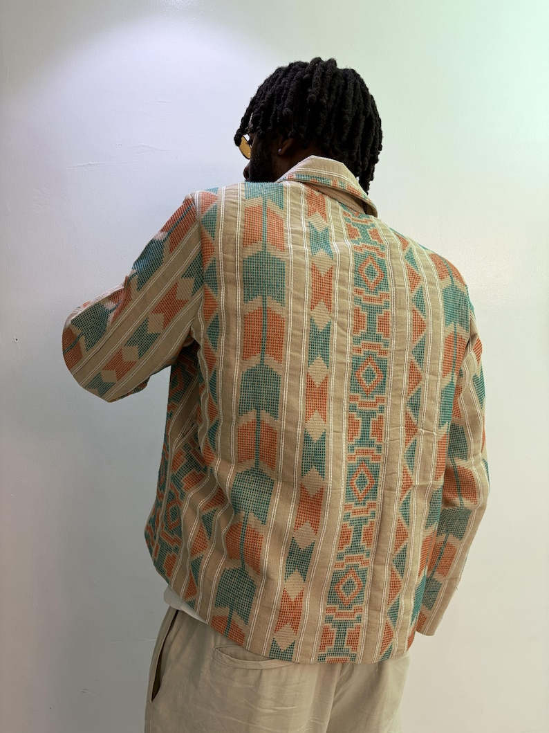 Puede incluir: Chaqueta beige con estampado geom&eacute;trico en naranja y verde azulado. El patr&oacute;n repite rayas verticales y formas de rombos. La chaqueta tiene cuello y mangas largas. La persona que lleva la chaqueta se ve por la espalda.