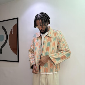 Puede incluir: Chaqueta con cremallera y estampado geom&eacute;trico en naranja, turquesa y beige. Se lleva con una camiseta blanca y pantalones beige. El estilo es casual y moderno. El dise&ntilde;o de la chaqueta es llamativo.
